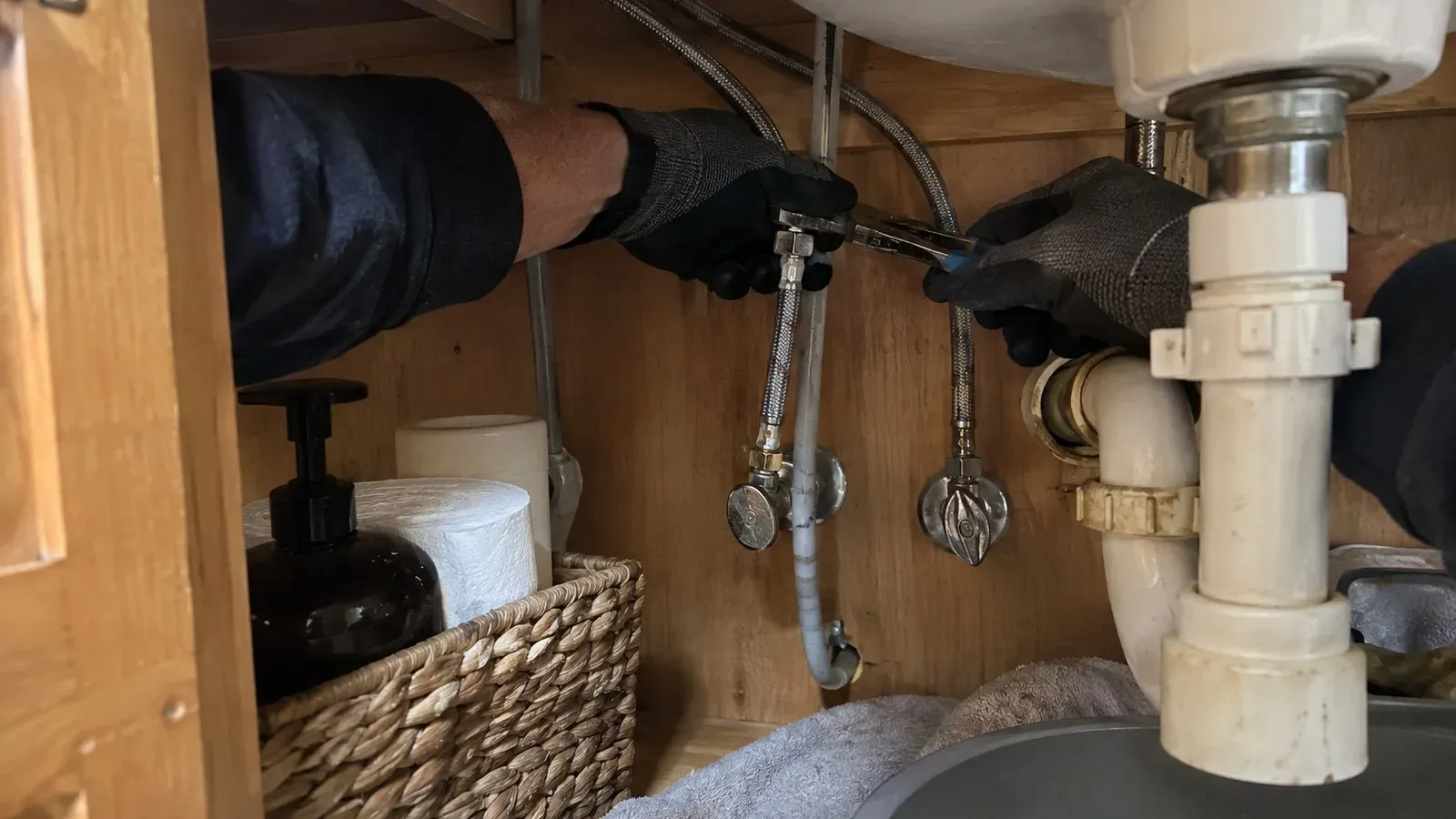Plumber tightening a sink drain trap under a bathroom vanity in a Southwest Portland home