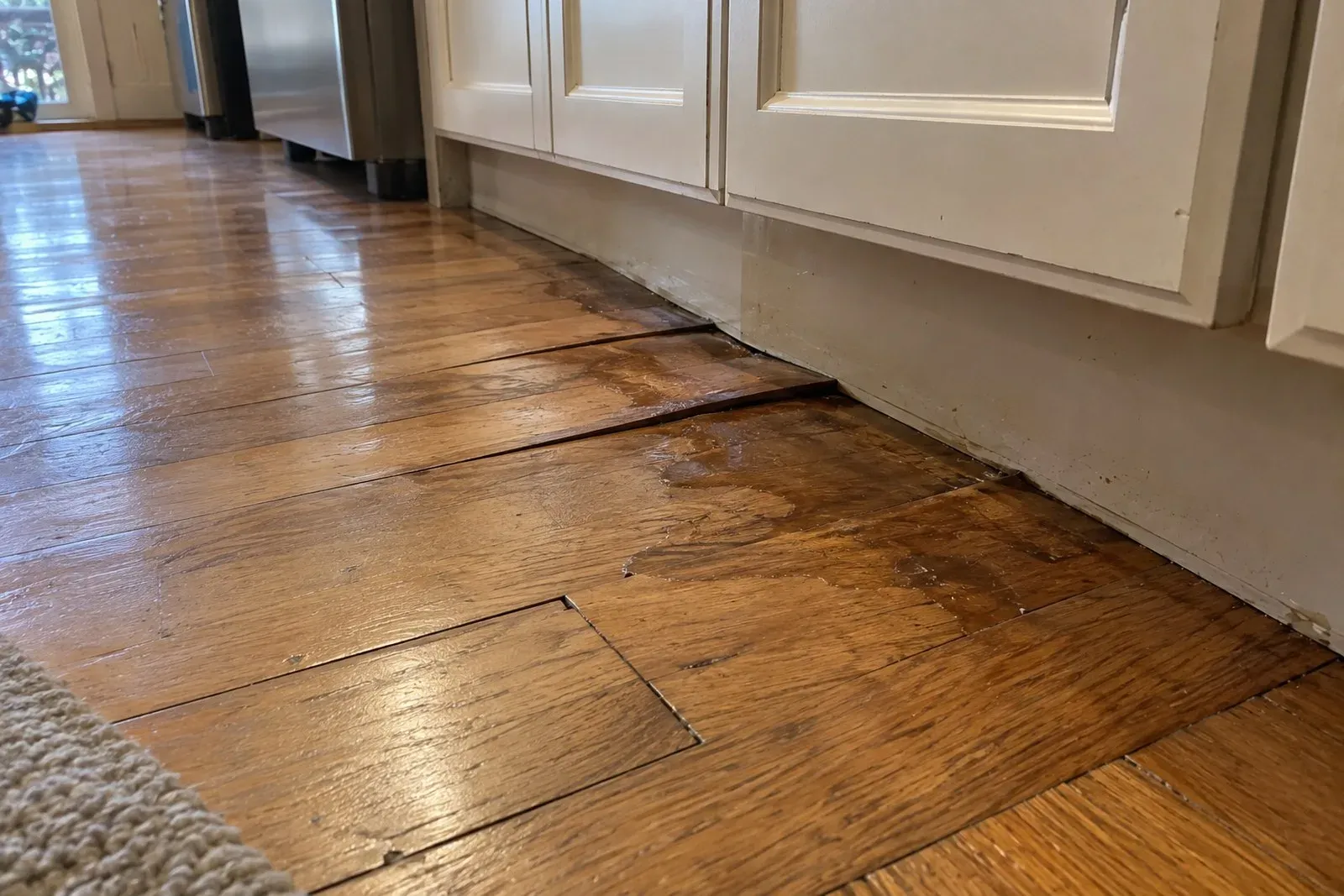 Cupped and warped hardwood floorboards near kitchen cabinets from a slow water leak