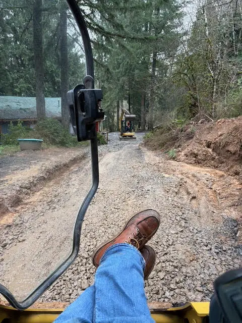 Wild Pine Plumbing operating a mini excavator on a rural Columbia County, Oregon driveway sewer project