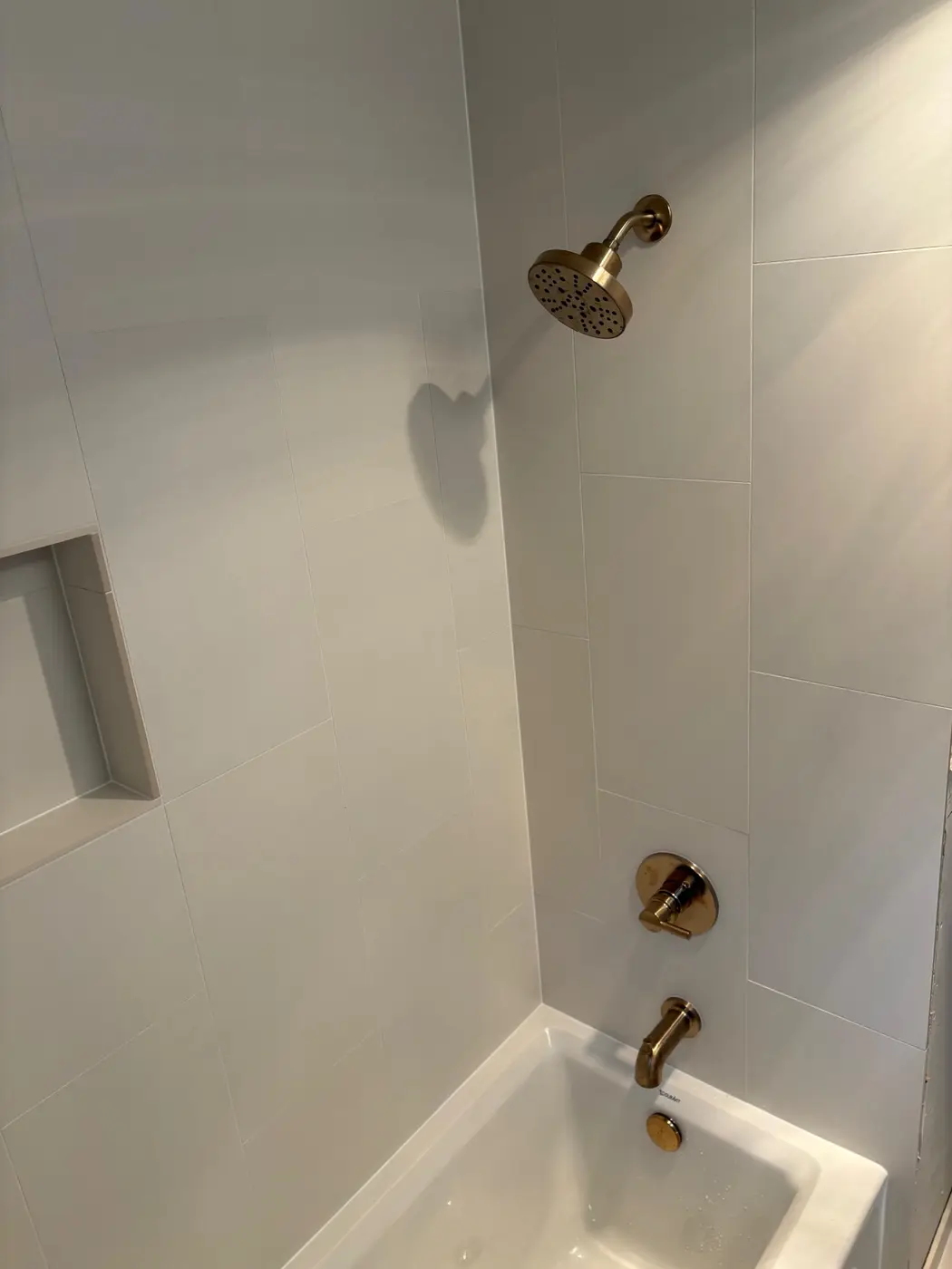 Modern white tile tub-shower with brushed gold trim by Wild Pine Plumbing serving Portland and St Helens, OR