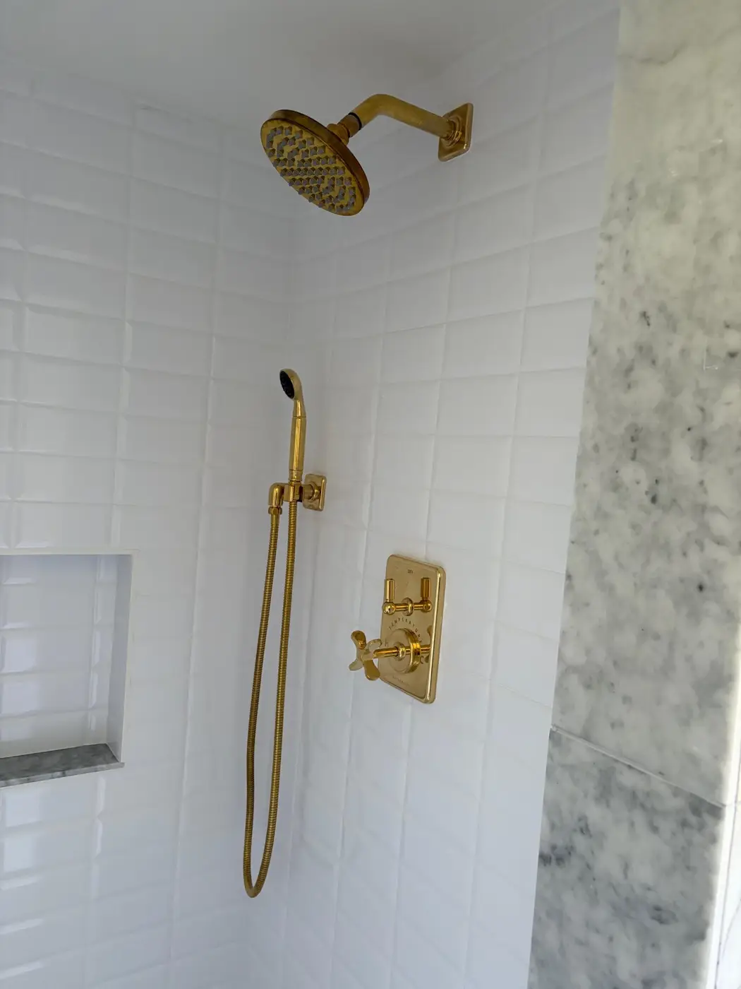 White beveled tile shower with brushed gold rainfall head, handheld, and cross-handle thermostatic valve by Wild Pine Plumbing in Portland, OR