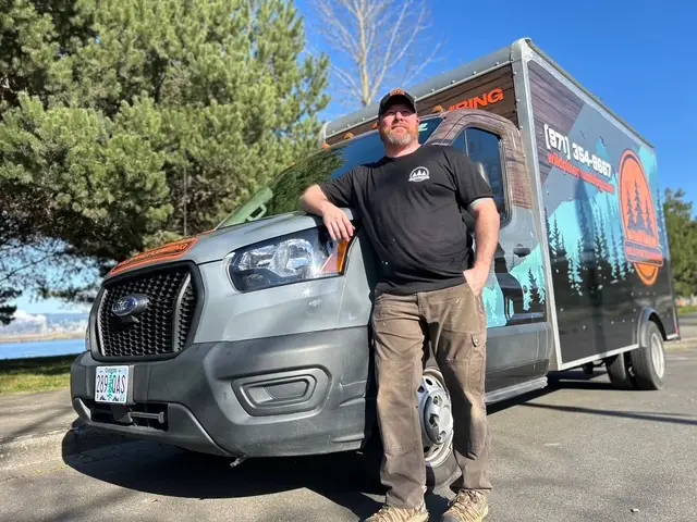Wild Pine Plumbing owner standing in front of the branded box truck along the Columbia River in St Helens, Oregon
